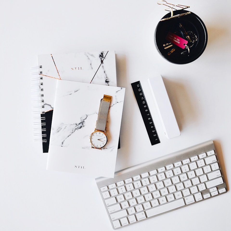 Apple Magic Keyboard near round gold-colored analog watch with silver-colored mesh band with notebook on white surface photography